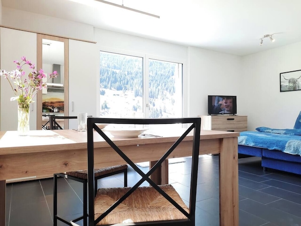A modern living space with a dining area, a TV, and a sofa.