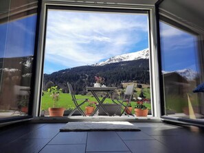 A balcony with a table and chairs, potted plants, and a view of a mountain landscape.