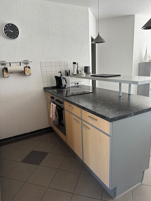 A modern kitchen with a central island, a hanging light fixture, and a clock on the wall. - Ideal for golfers, cyclists, and recreational athletes—3-room apartment in a central location (Krauchenwies)