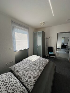 A bedroom with a bed, a wardrobe, a mirror, and a window with blinds. - Ideal for golfers, cyclists, and recreational athletes—3-room apartment in a central location (Krauchenwies)