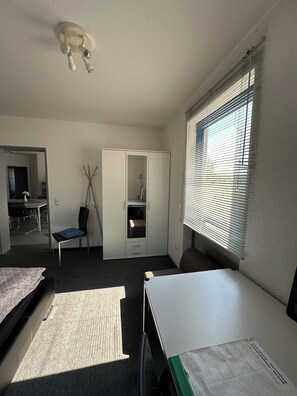 A room with a bed, a desk, a chair, a wardrobe, and a window with blinds. - Ideal for golfers, cyclists, and recreational athletes—3-room apartment in a central location (Krauchenwies)