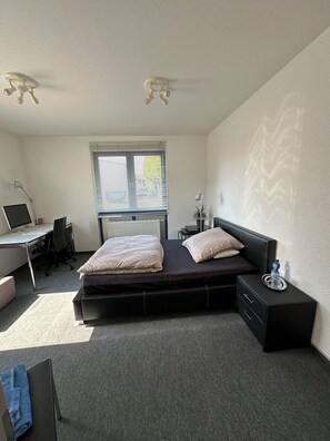 Quarto com cama, escrivaninha, cadeira, radiador e janela com persianas.