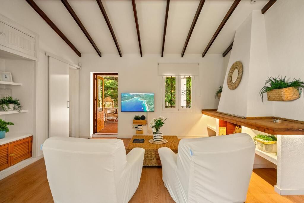Une pièce avec un téléviseur, une table basse en bois et des chaises blanches.