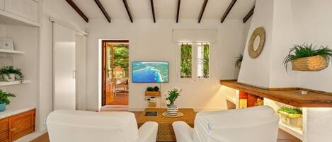 A room with a television, a wooden coffee table, and white chairs.