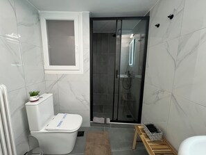 A bathroom with a toilet, a shower enclosure, and a small wooden stool.