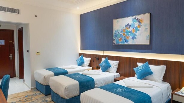 A hotel room with three beds, a painting on the wall, and a desk with a chair.