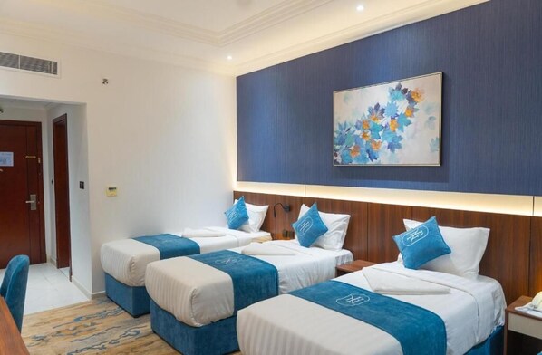 A hotel room with three beds, a painting on the wall, and a desk with a chair.