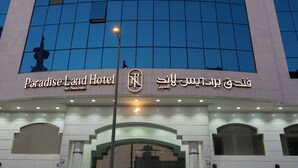 The exterior of the Paradise Land Hotel with a modern architectural design, featuring a prominent entrance and a large glass facade reflecting the sky.