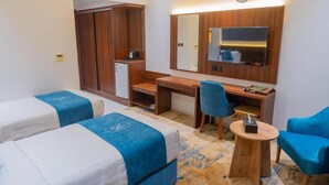A hotel room with two beds, a desk, a chair, a small table, a mirror, and a clock on the wall.