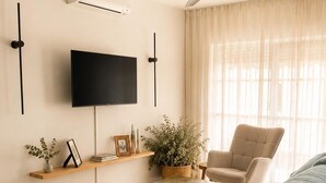 Ein Wohnzimmer mit einer Couch, einem Couchtisch, einem Fernseher, einem Deckenventilator und einem fenster mit Vorhängen.