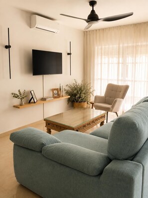 Ein Wohnzimmer mit einer Couch, einem Couchtisch, einem Fernseher, einem Deckenventilator und einem fenster mit Vorhängen.