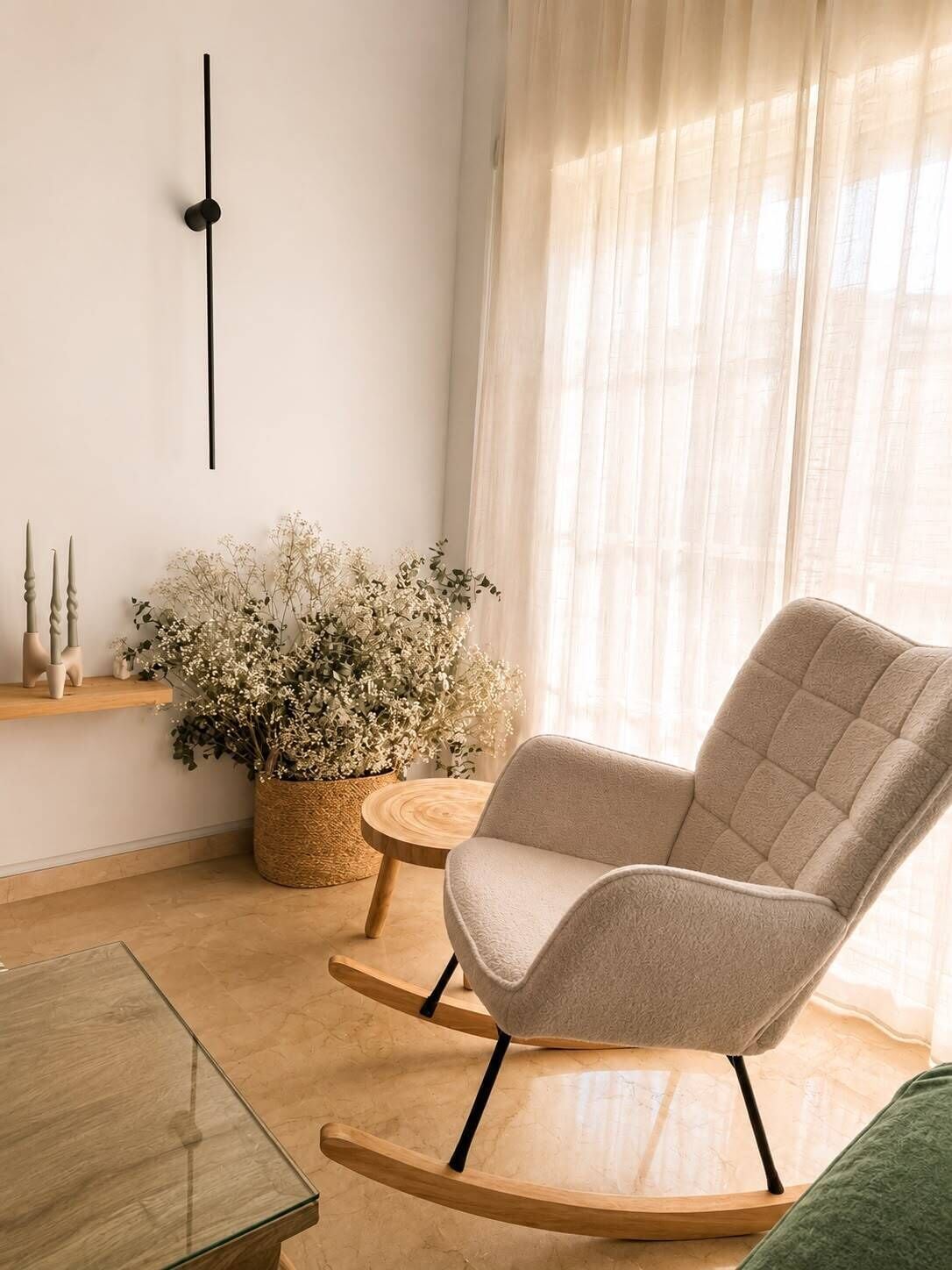 A room with a rocking chair, a small wooden table, a potted plant, and a wall clock.