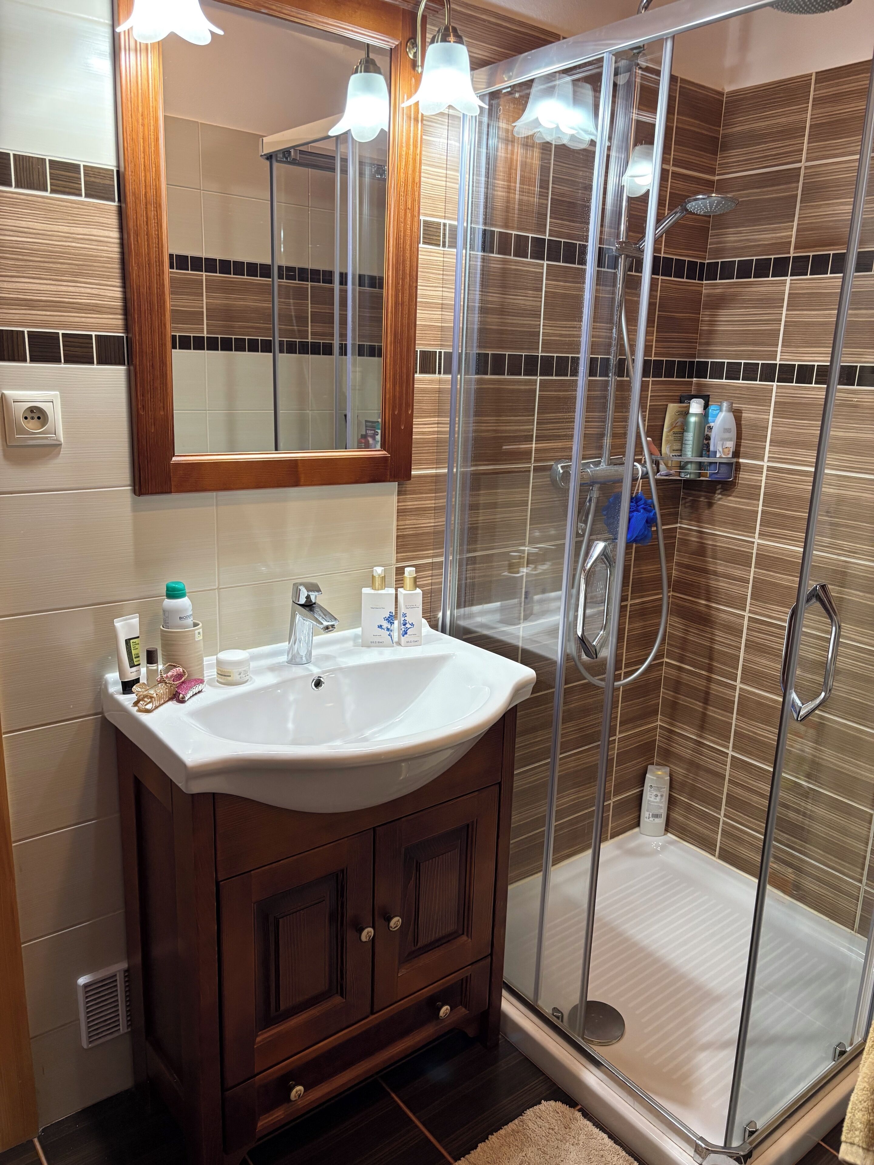 Une salle de bain avec un meuble-lavabo en bois, une cabine de douche en verre et un miroir au-dessus du lavabo.