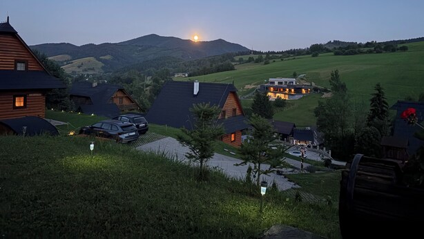 Ein ländliches Dorf mit traditionellen Holzhäusern, blauem Himmel und einem Berg im Hintergrund.