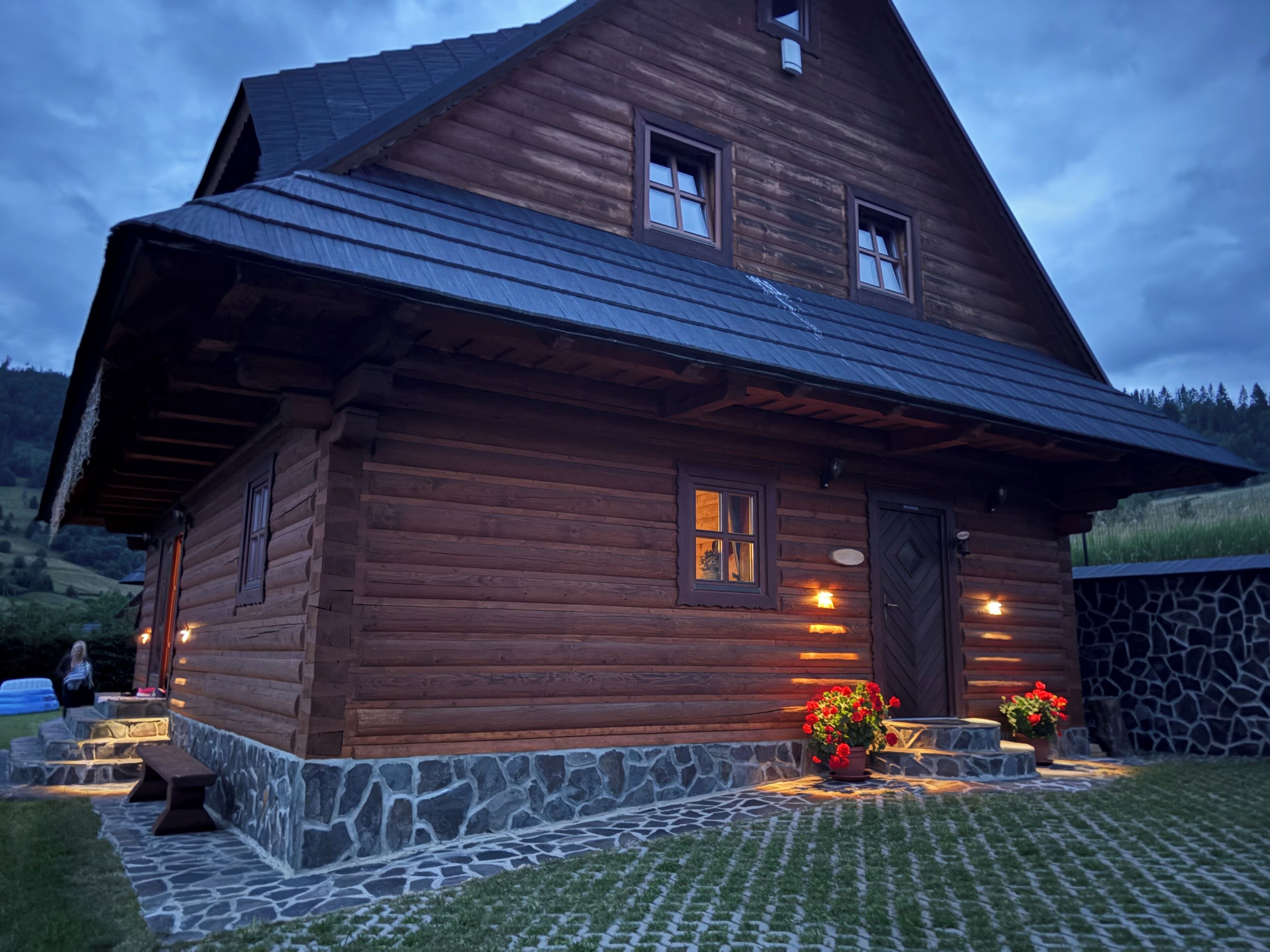 A wooden cabin with a stone foundation, a porch with a bench, and potted plants.