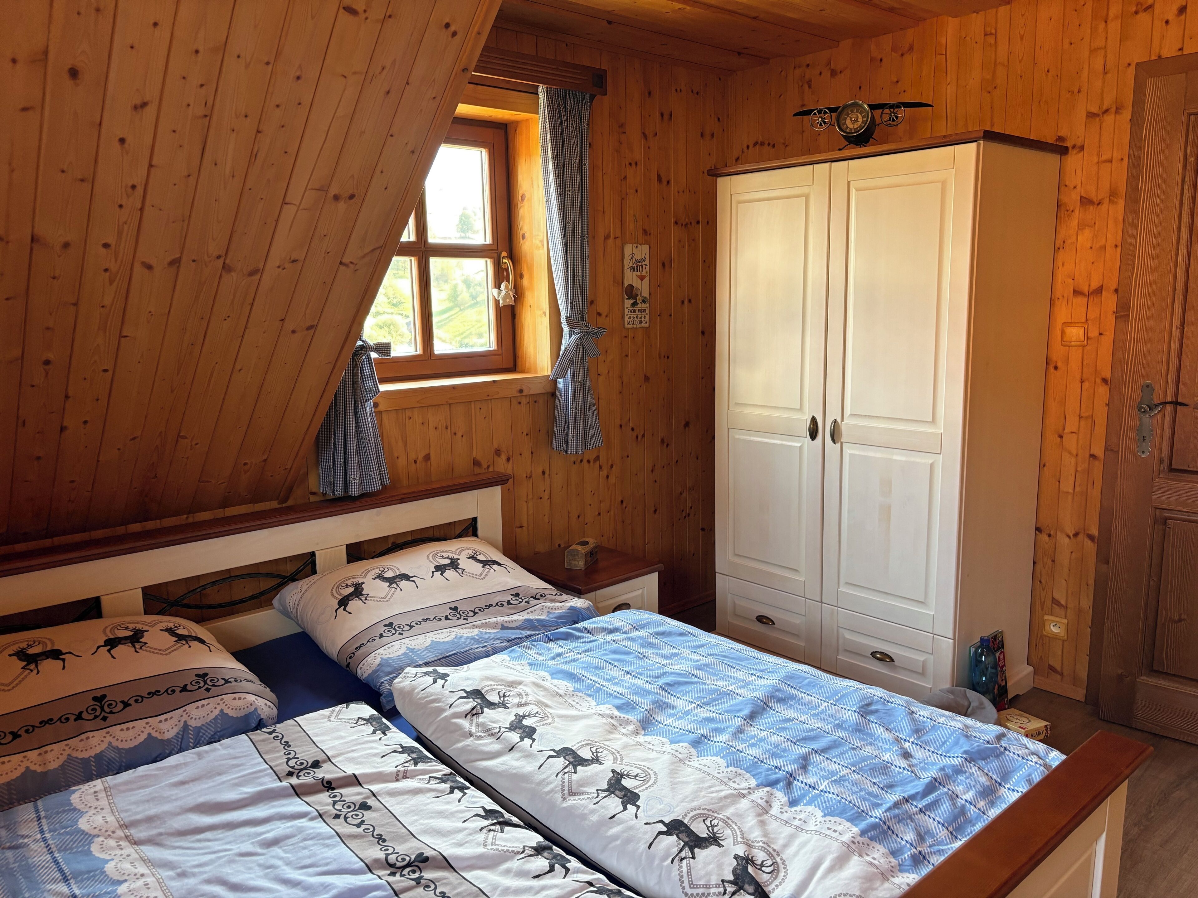 Ein Schlafzimmer einer Holzhütte mit zwei Betten, einem Kleiderschrank und einem Fenster mit Vorhängen.