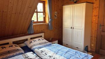 Ein Schlafzimmer einer Holzhütte mit zwei Betten, einem Kleiderschrank und einem Fenster mit Vorhängen.