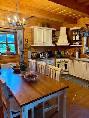 A wooden interior with a dining table, chairs, a chandelier, cabinets, and a window with a view.