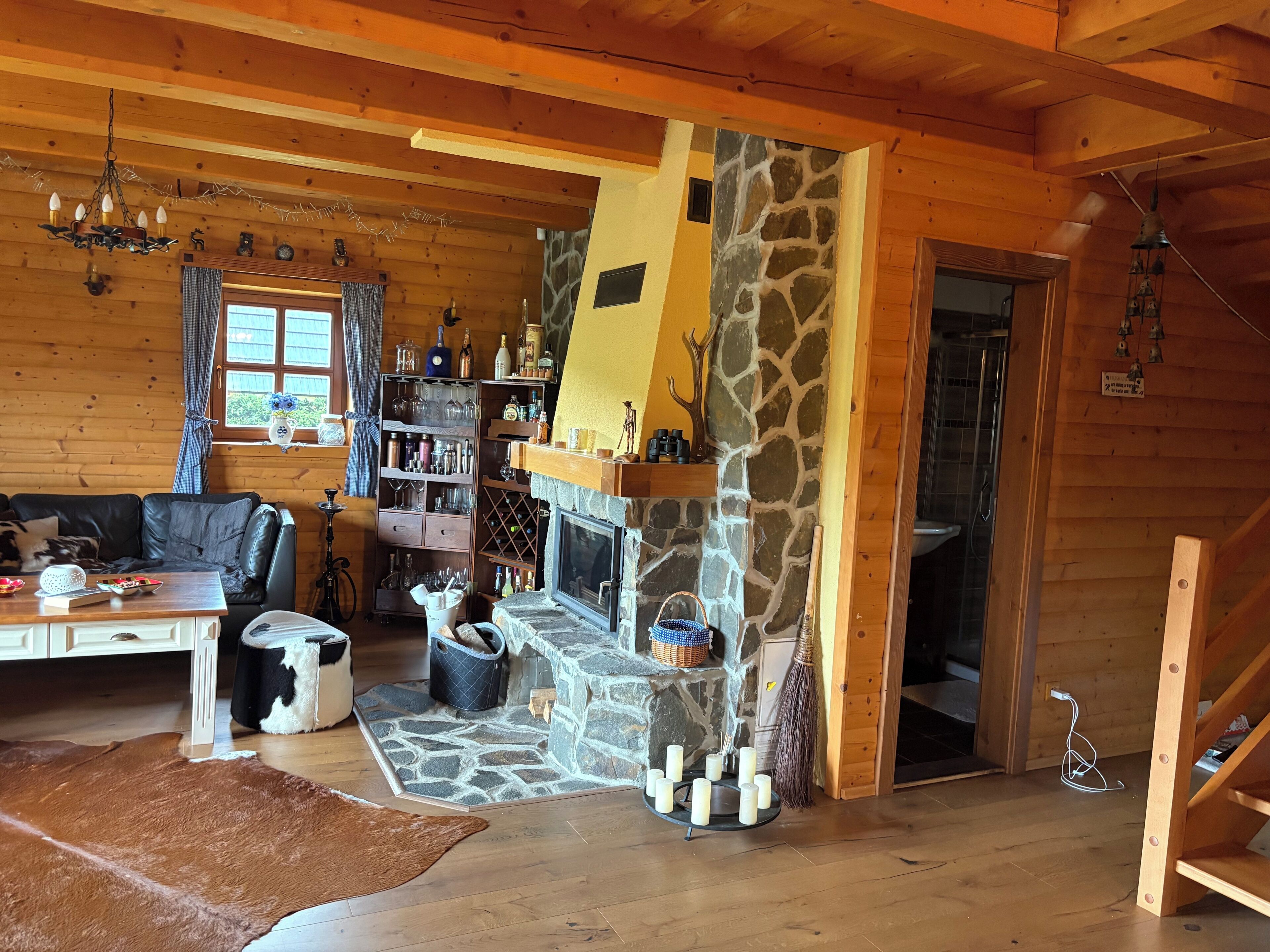En mysig stuga med en inmurad steneldstad, träväggar, en lädersoffa och en matplats.