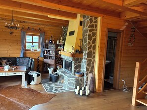 A cozy cabin interior with a stone fireplace, wooden walls, a leather sofa, and a dining area.