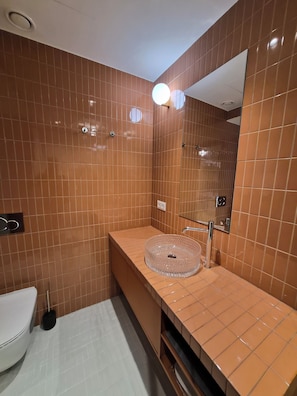Ein Badezimmer mit einem runden Glaswaschbecken, einem Spiegel und einer Toilette.