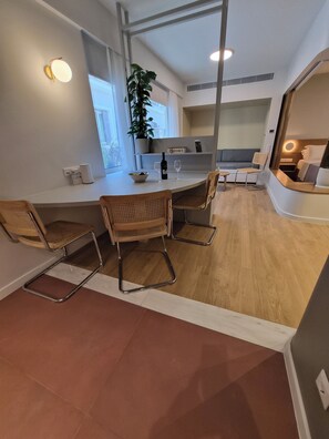 A modern interior with a dining area featuring a round table, four chairs, a potted plant, and a built-in bench. - Apollonos 26 Luxury Suite (Athina)