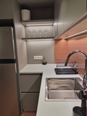 Eine kompakte Küche mit einem Edelstahlkühlschrank, einer Spüle mit modernem Wasserhahn und einem Weinkühlschrank über der Arbeitsfläche.