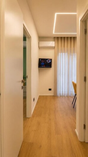 A hallway with a wooden floor, a mounted TV, and a door leading to another room.