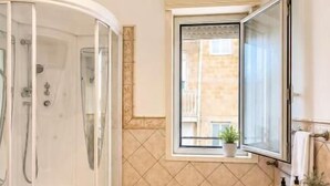 Un baño moderno con ducha de vidrio, lavamanos con espejo y ventana que proporciona luz natural.