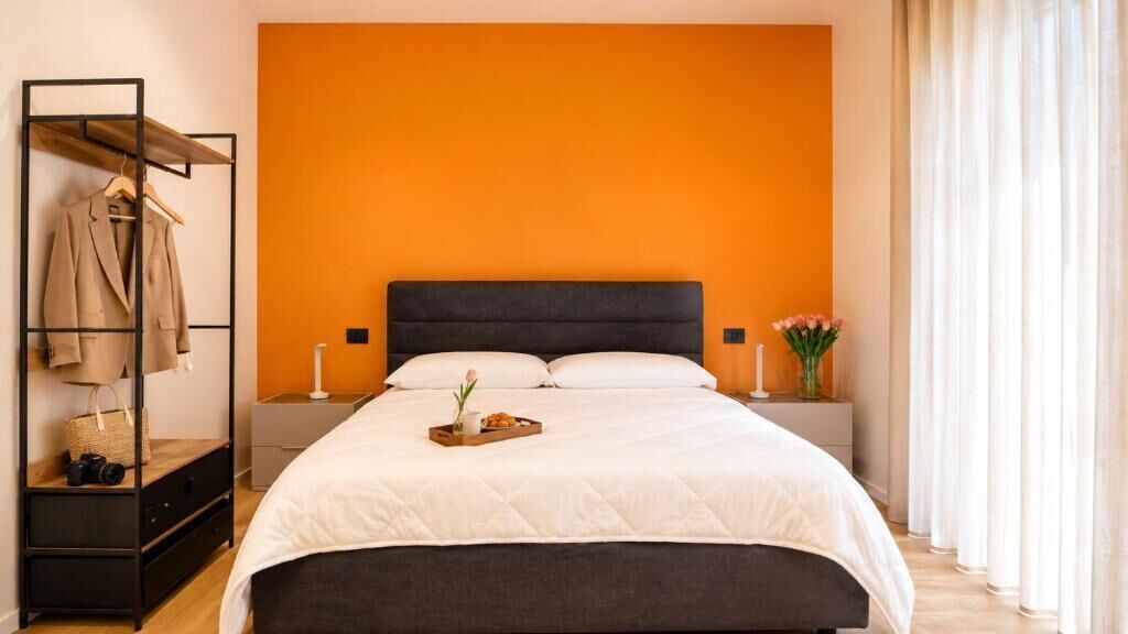 A neatly made bed with a dark headboard, a bedside table with a lamp, and a clothing rack with a coat.