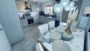 A modern kitchen with a dining area, featuring a marble table, white chairs, and a unique light fixture. - Room-stylish Modern Double Room With pri (Peterborough)