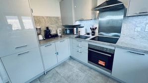 A modern kitchen with white cabinets, a stainless steel range hood, a built-in oven, and a coffee maker. - Room-stylish Modern Double Room With pri (Peterborough)