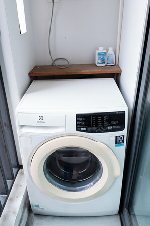 Een compacte wasmachine met een bedieningspaneel, een houten plank erboven en twee flessen wasmiddel.