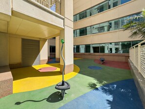 A multi-level building with a children's play area featuring colorful ground surfaces and a swing set. - Downtown Dubai Escape | 1BR at 29 Boulevard (Dubai)
