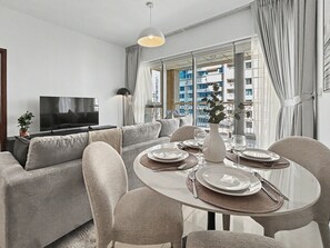 A modern living room with a sofa, dining table set for four, and a TV. - Downtown Dubai Escape | 1BR at 29 Boulevard (Dubai)