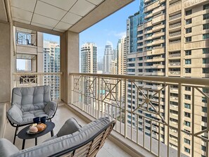 A balcony with a cushioned seating area, a small table with a cup and pastries, and a view of high-rise buildings. - Downtown Dubai Escape | 1BR at 29 Boulevard (Dubai)