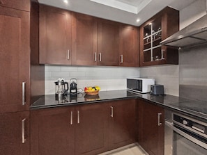 A modern kitchen with dark brown cabinetry, a black countertop, and stainless steel appliances including a microwave and oven. - Downtown Dubai Escape | 1BR at 29 Boulevard (Dubai)