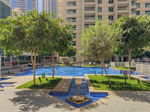 A swimming pool with a tiled edge, surrounded by trees and a building in the background. - Downtown Dubai Escape | 1BR at 29 Boulevard (Dubai)