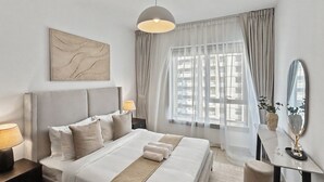 Een moderne hotelkamer met een groot bed, bedlampen, een bureau met spiegel en uitzicht op de stad door dunne gordijnen.