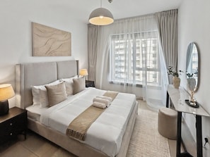 A modern hotel room with a large bed, bedside lamps, a desk with a mirror, and a view of the city through sheer curtains. - 29 Boulevard T1 - 1801 1BD (Dubai)