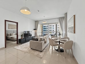 A modern living room with a sofa, TV, and dining area with chairs and a table. - 29 Boulevard T1 - 1801 1BD (Dubai)