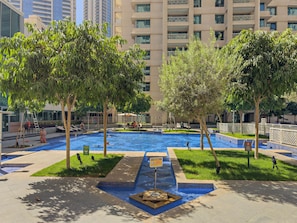 A swimming pool area with multiple pools, surrounded by trees and a building in the background. - 29 Boulevard T1 - 1801 1BD (Dubai)