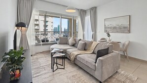 Een moderne woonkamer met een grijze bank, een bijzettafeltje, een potplant en uitzicht op de stad door grote ramen.