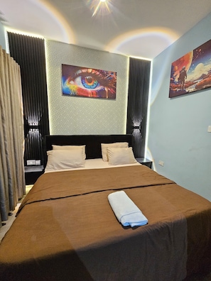 A hotel room with a large bed, a headboard with a geometric pattern, and two wall-mounted paintings. - Eastlands - 1 bedroom apartment, Lekki Phase 1. (Lekki)