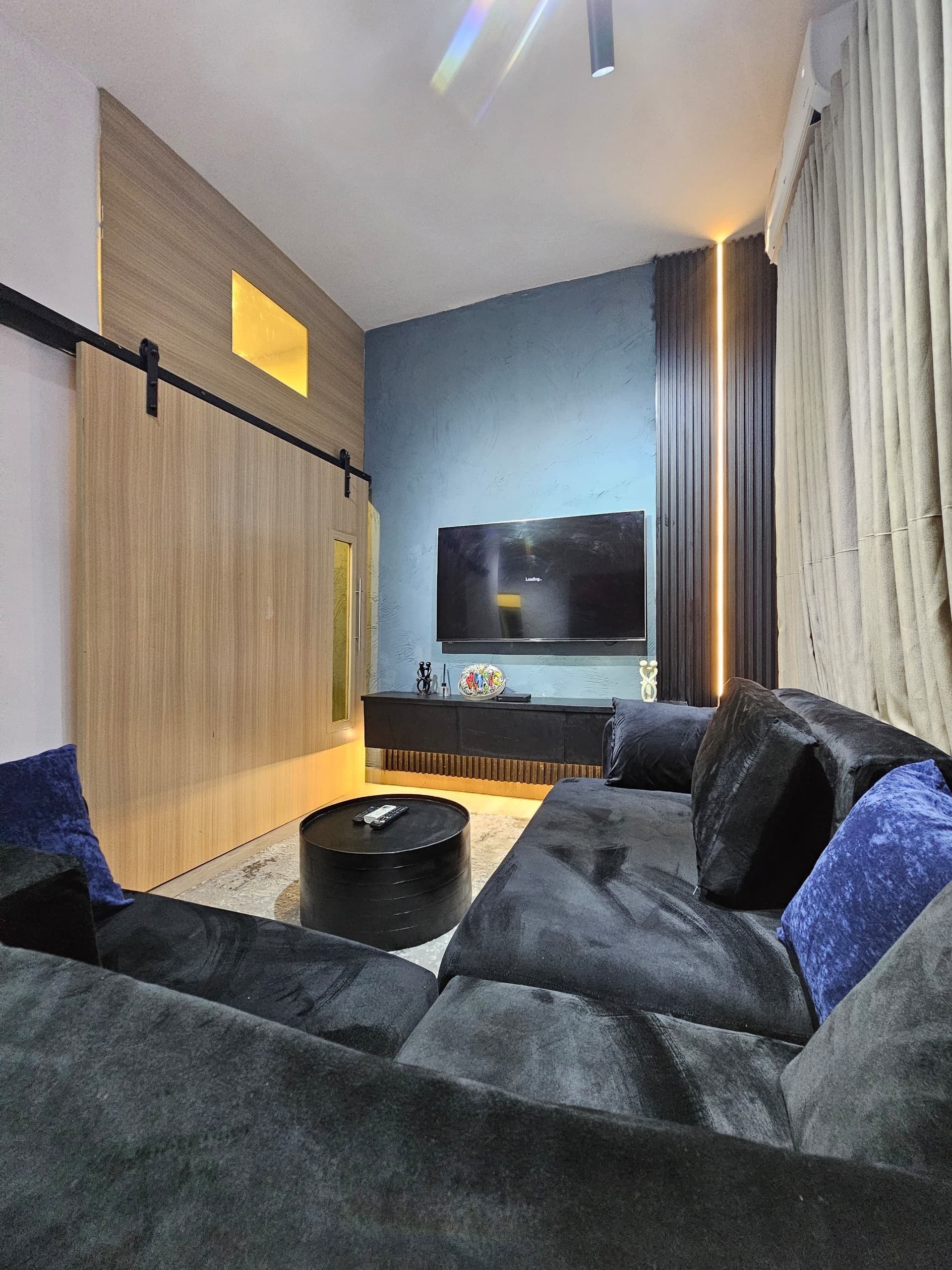 A modern living room with a large flat-screen TV, a dark-colored sofa, and a coffee table.