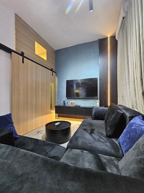 A modern living room with a large flat-screen TV, a dark-colored sofa, and a coffee table. - Eastlands - 1 bedroom apartment, Lekki Phase 1. (Lekki)
