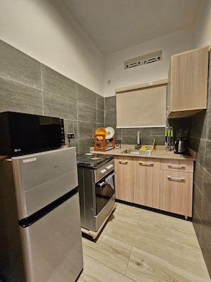 A compact kitchen with a refrigerator, stove, and microwave. - Eastlands - 1 bedroom apartment, Lekki Phase 1. (Lekki)