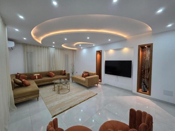 A modern living room with a sofa set, a coffee table, and a flat-screen TV mounted on the wall.