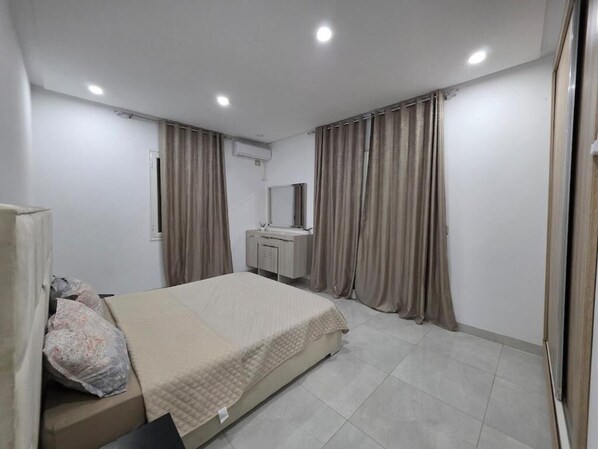 Un dormitorio con cama, cortinas, tocador y ventana.