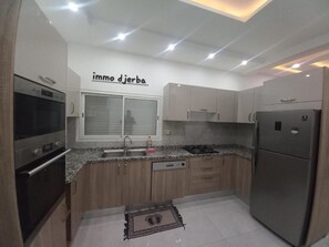 A modern kitchen with a built-in oven, a refrigerator, and a window with a view. - Dream villa with a private pool and 3 suites (Djerba)